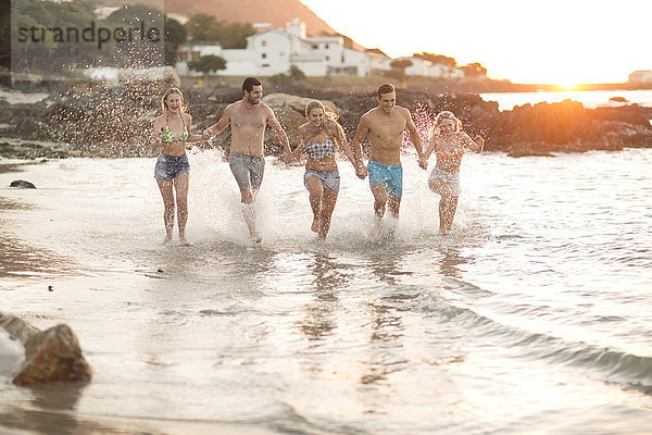 Fünf Freunde  die in Wellen am Strand rennen.