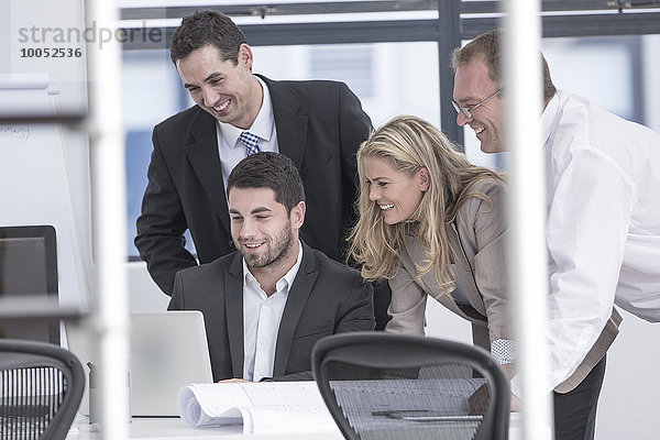 Lächelnde Geschäftsleute im Büro mit Blick auf den Laptop