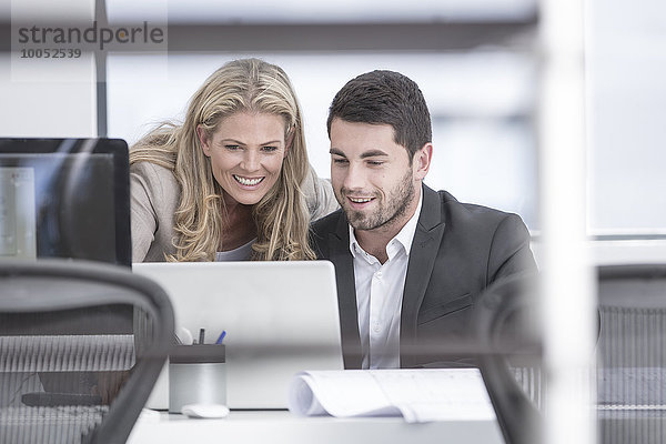 Lächelnder Geschäftsmann und Geschäftsfrau im Büro mit Blick auf Laptop