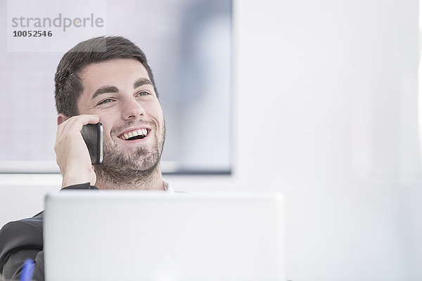 Lächelnder Geschäftsmann im Büro mit Laptop und Handy