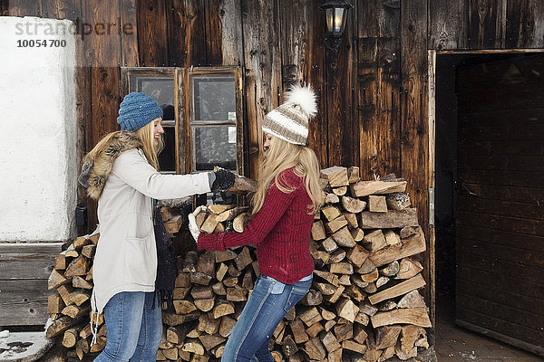 Zwei junge Freundinnen stapeln Baumstämme vor der Hütte