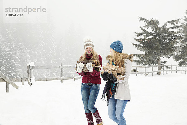 Zwei junge Freundinnen mit Baumstämmen im Schnee