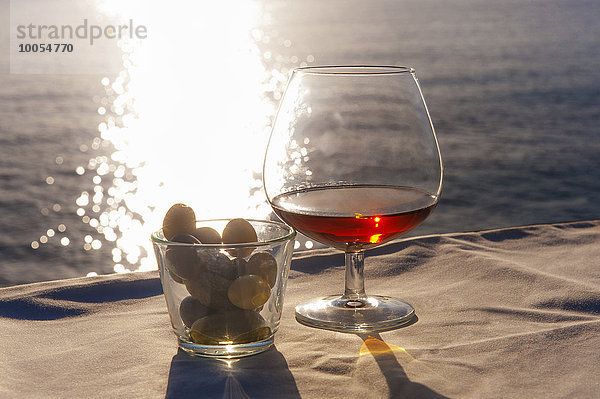 Schnapsglas und Oliven auf sonnigem Tisch an der Küste