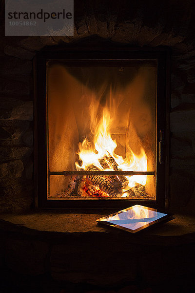 Glühendes Holzfeuer und digitales Tablett auf dem Herd