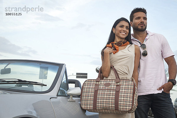 Porträt eines mittleren erwachsenen Paares  das an einem Cabriolet steht.