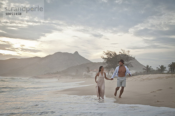 Mittleres erwachsenes Paar läuft am Strand entlang  Hand in Hand