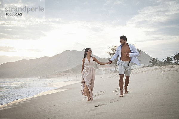 Mittleres erwachsenes Paar  das am Strand entlanggeht  Hand in Hand