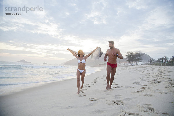 Mittleres erwachsenes Paar  das in Badebekleidung am Strand entlang läuft.