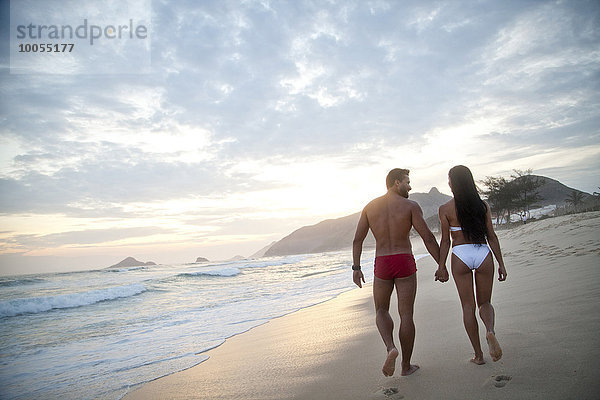Mittleres erwachsenes Paar am Strand entlang  Hand in Hand  in Badebekleidung  Rückansicht