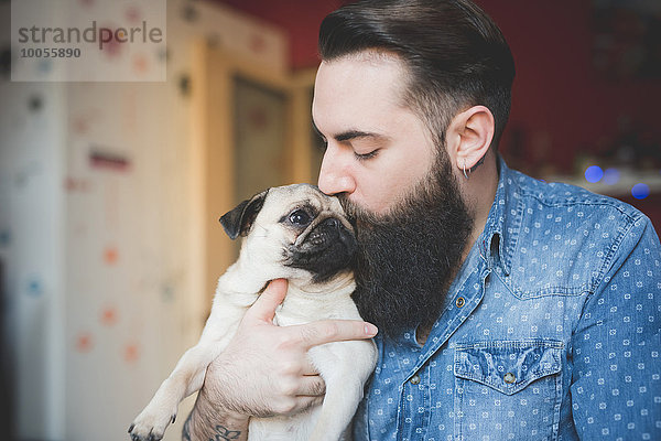 Junger bärtiger Mann küsst Hund in den Armen