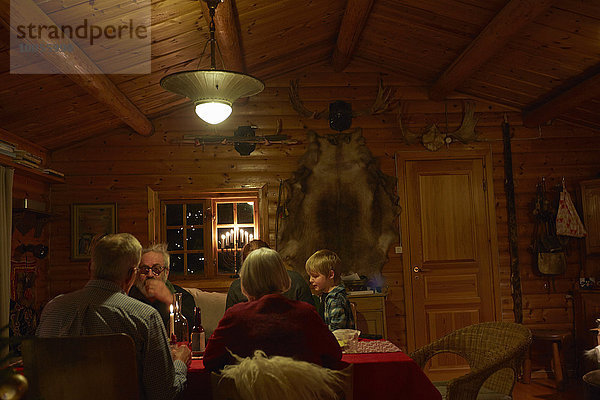 Drei Generationen Familie sitzen am Weihnachtstisch in der Blockhütte in der Nacht