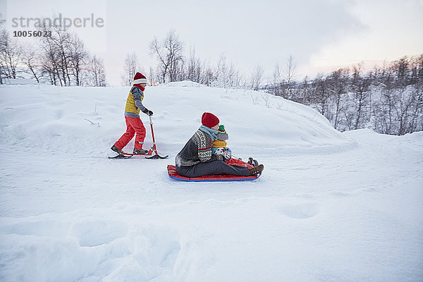 Mutter und zwei Söhne auf Schlitten und Schneeroller auf schneebedecktem Hügel  Hemavan  Schweden