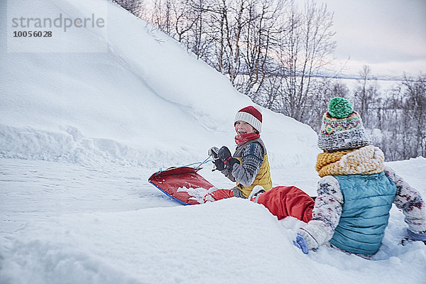 Zwei Brüder auf Schlitten auf schneebedecktem Hügel  Hemavan  Schweden