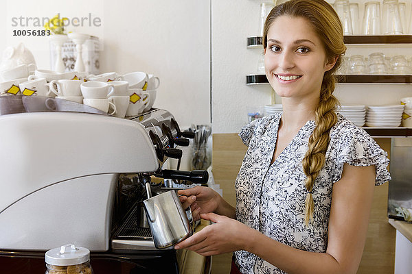 Junge Frau mit Kaffeemaschine beim Blick in die Kamera  Porträt