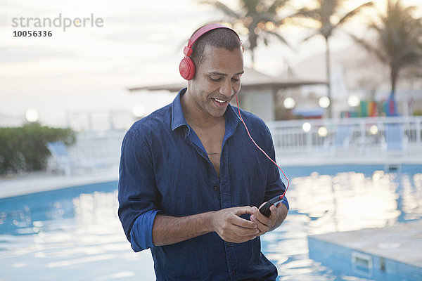 Mittlerer Erwachsener Mann  der Smartphone-Musik am Pool des Hotels  Rio De Janeiro  Brasilien  auswählt.