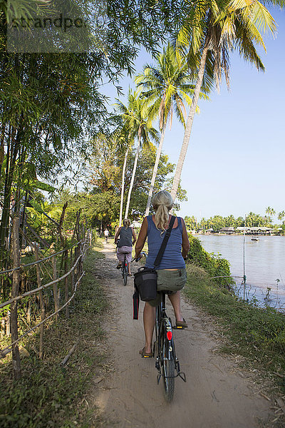 Rückansicht von zwei weiblichen Touristen  die am Mekong-Flussufer  Don Det  Laos radeln
