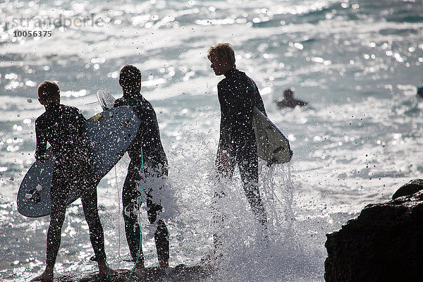 Drei silhouettierte männliche Surfer auf Seefelsen  Fuerteventura  Spanien