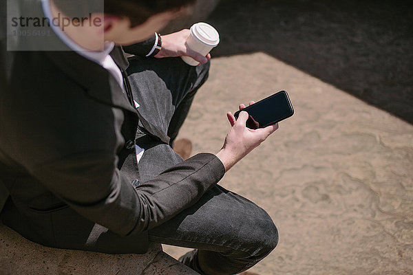 Über die Schulter des jungen Geschäftsmannes beim Lesen von Smartphone-Texten