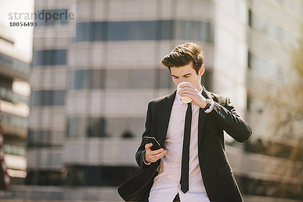 Ein junger Geschäftsmann  der Kaffee trinkt  während er Smartphone-Texte liest.