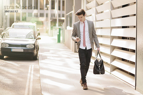 Ein junger Geschäftsmann liest Smartphone-Texte  während er außerhalb des Büros spazieren geht.
