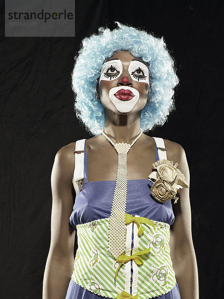 Atelierporträt einer jungen Frau mit Clown-Gesichtsfarbe und blauer Perücke  die aufschaut