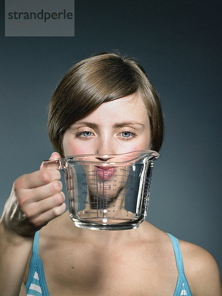 Atelierporträt einer jungen Frau  die eine Glasmesskanne vor das Gesicht hält.