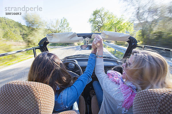 Zwei reife Frauen  Händchen haltend  im Cabriolet  Rückansicht