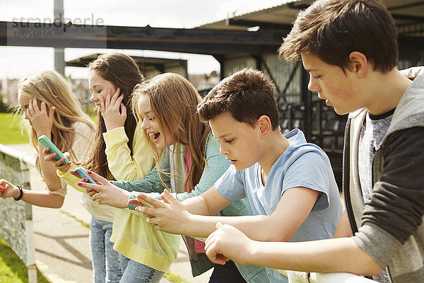 Fünf Mädchen und Jungen in der Stadiontribüne lesen Smartphones