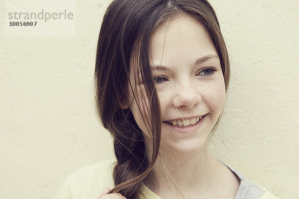 Porträt eines lächelnden Mädchens mit geflochtenen Haaren vor der Wand