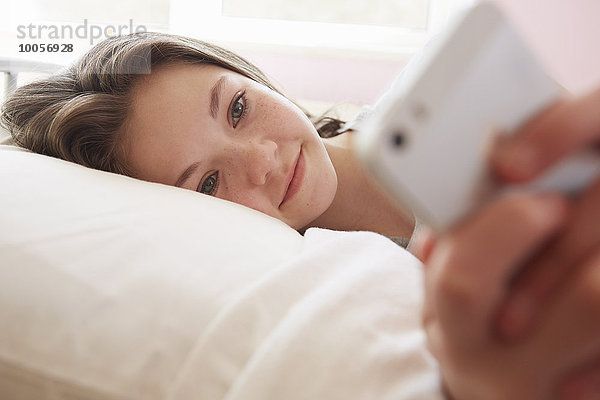 Mädchen auf dem Bett liegend SMS auf dem Smartphone