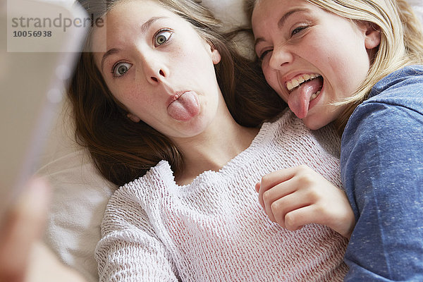 Zwei Mädchen  die auf dem Bett liegen und Zungen für Smartphone Selfie herausstrecken.