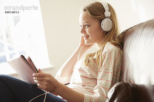 Mädchen auf dem Sofa trägt Kopfhörer und hört Musik vom digitalen Tablett.
