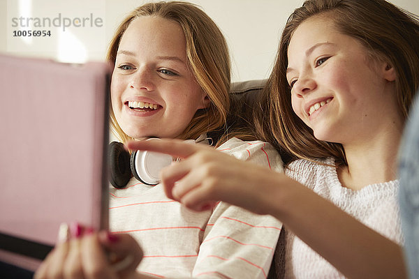 Zwei Mädchen auf dem Sofa lachend und zeigend auf digitales Tablett