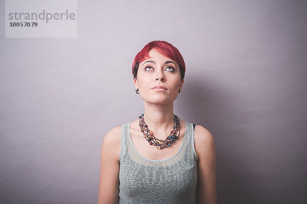 Studio-Porträt einer jungen Frau mit kurzen rosa Haaren nach oben schauend