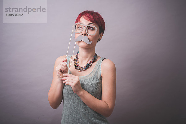 Atelierporträt einer jungen Frau mit Brille und Schnurrbart vor dem Gesicht