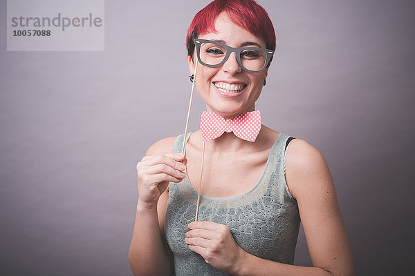 Atelierporträt einer verwirrten jungen Frau  die eine Brille vor dem Gesicht hält.