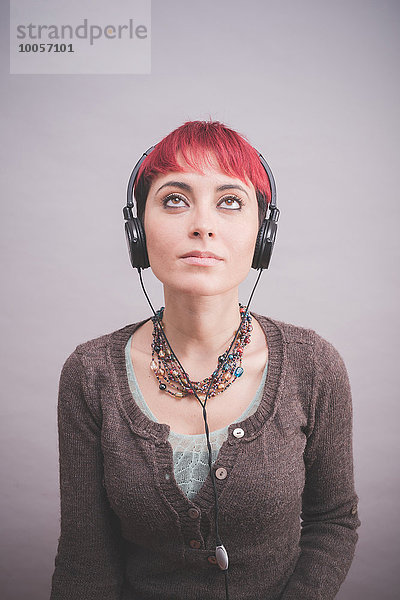 Studio-Porträt einer jungen Frau mit kurzen rosa Haaren und Kopfhörern