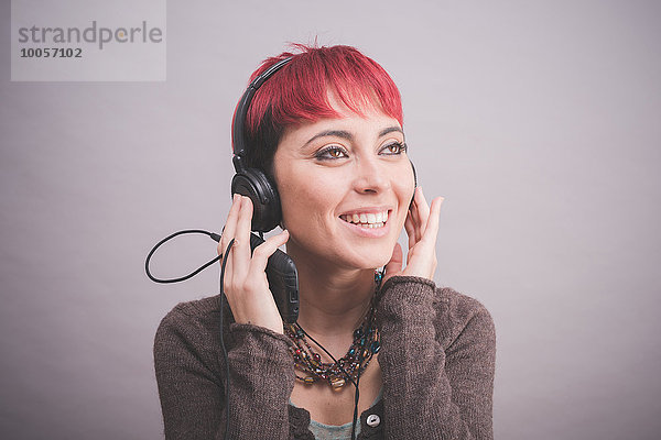 Studio-Porträt einer jungen Frau mit kurzen rosa Haaren  die Kopfhörer hört.