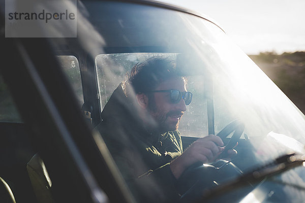 Mann mit Sonnenbrille fährt Auto im Sonnenlicht
