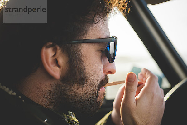 Nahaufnahme eines erwachsenen Mannes im Auto beim Anzünden einer Zigarette