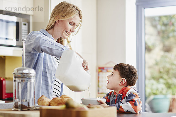Mutter gießt Milch in die Frühstücksschale des Sohnes.