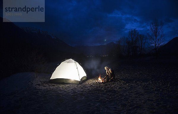 Mann am Lagerfeuer und Zelt bei Nacht