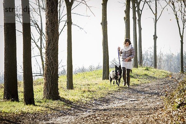 Mittlere erwachsene Frau  die mit ihrem Hund auf einem Feldweg spazieren geht.