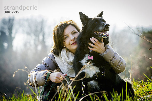 Porträt einer mittleren erwachsenen Frau mit Arm um ihren Hund im Feld