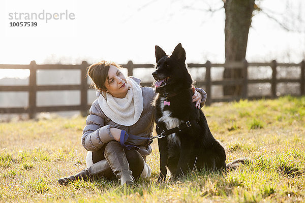 Mittlere erwachsene Frau sitzend mit ihrem Hund im Feld