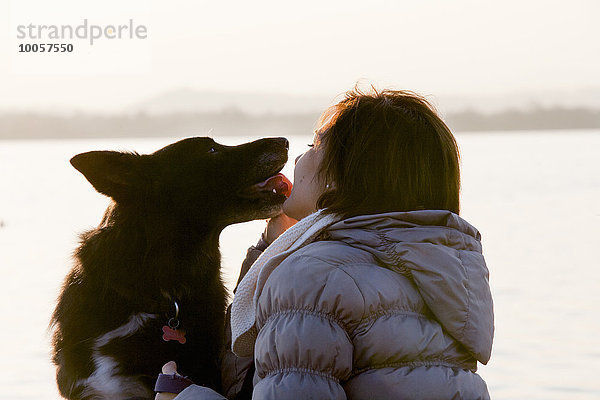 Hund leckt mittlere erwachsene Frauen Gesicht am Seeufer