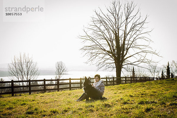 Mittlere erwachsene Frau und ihr Hund sitzend im Seeuferfeld