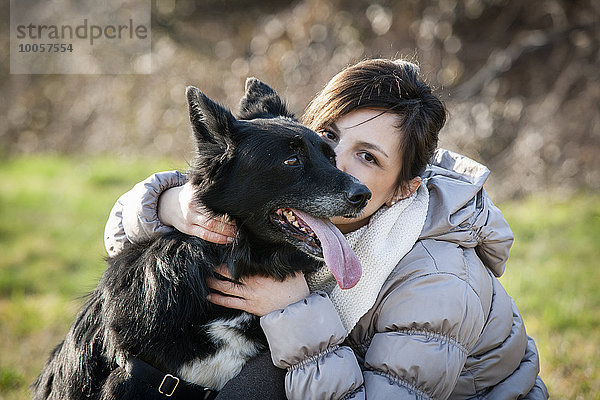 Porträt einer mittleren erwachsenen Frau  die ihren Hund auf dem Feld küsst.