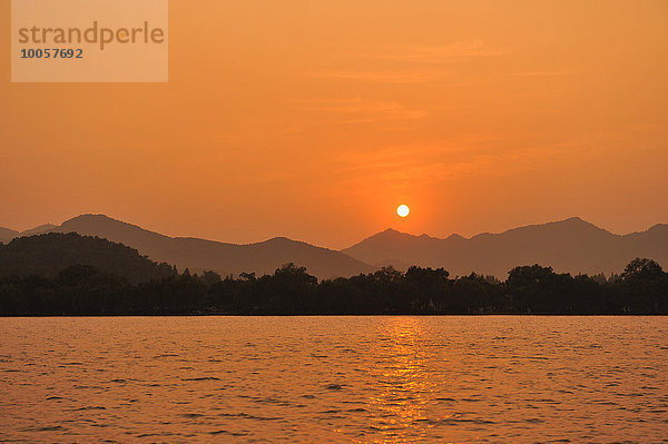 Sonnenuntergang über dem See  Berge in der Ferne  Hangzhou  China