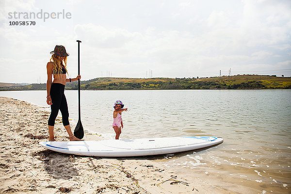 Mittlere erwachsene Frau und Kleinkind Tochter mit Paddelbrett am Strand  Carlsbad  Kalifornien  USA